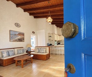 A living room with a sofa set, a coffee table, and a dining area with chairs. - Artemis Sea Cottage - Near beach & airport by ΜΡS (Artemis)