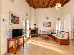A living room with a fireplace, a television, a sofa, and a dining table. - Artemis Sea Cottage - Near beach & airport by ΜΡS (Artemis)