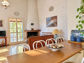Un comedor con una mesa de madera, sillas blancas, un tazón de comida, una chimenea y un televisor.