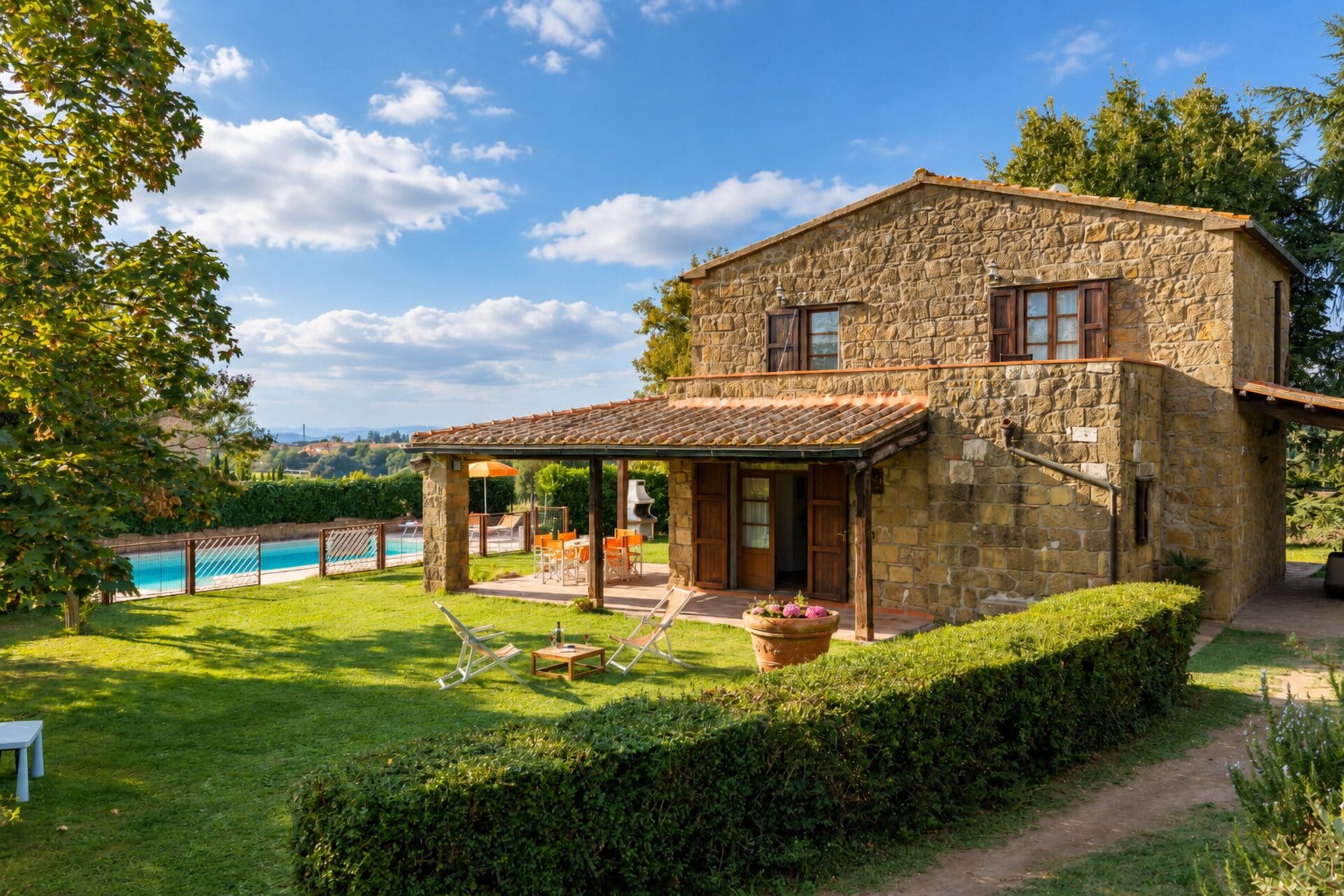 A stone house with a pool, a covered patio, and a well-maintained lawn.