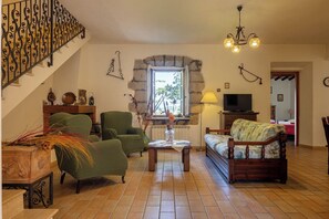 Una sala de estar con pared de piedra, una escalera, chimenea y televisor.