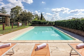 A rectangular swimming pool with a clear blue water surface, surrounded by a low stone wall and a metal fence. There are lounge chairs with towels placed on them, and the area is enclosed by a hedge. - Ortale a Pitigliano with Pool (Pitigliano)