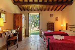 A room with a wooden desk, two beds with red bedding, a wardrobe, and a view of greenery outside. - Ortale a Pitigliano with Pool (Pitigliano)