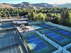 Un complex de pistes de tennis amb diverses pistes, zones d'estar i vistes a les muntanyes de fons.
