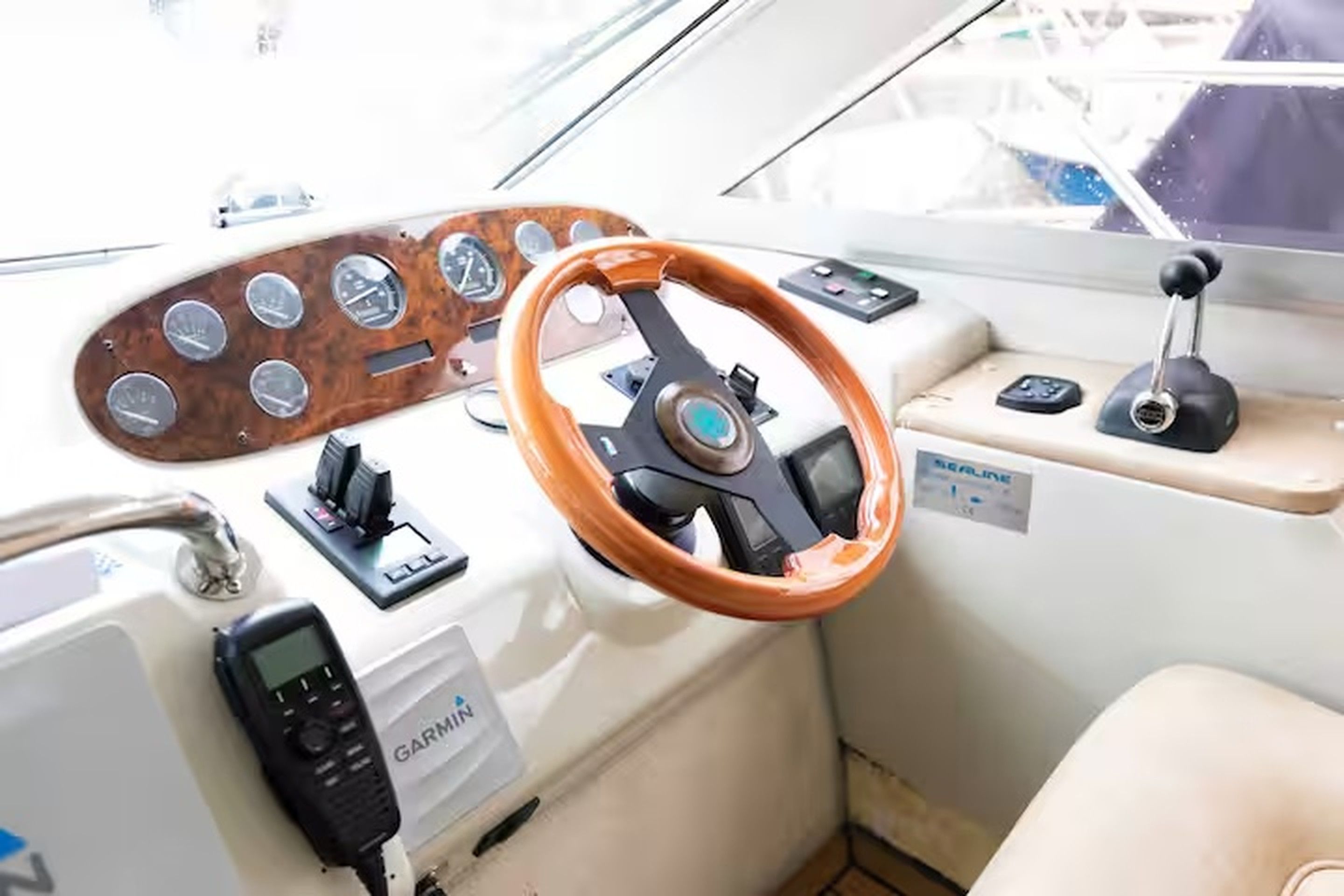 Taulell de comandament d'una embarcació amb un timó de fusta, un dispositiu Garmin i canvi manual.