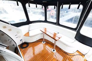 Interno di una barca con un ponte in legno, una cabina bianca e finestre a cornice nera.