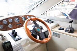 Pannello di controllo di una barca con timone in legno, indicatori e dispositivo Garmin.