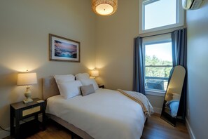 A neatly made bed with white linens and pillows, a bedside table with a lamp, a framed picture on the wall, and a window with curtains. - 1 Mi to Floyd Country Store: Cozy Mtn Cottage (Floyd)