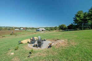 Un espace extérieur verdoyant, doté d’un foyer, de sièges et offrant une vue sur un paysage rural.