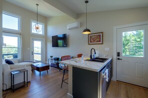 A modern kitchen with a marble countertop, a dining area with a sofa and chairs, and a large window with a view of trees. - 1 Mi to Floyd Country Store: Cozy Mtn Cottage (Floyd)