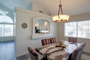 A dining area with a marble table, cushioned chairs, a pendant light, and a wall-mounted mirror. - Private Pool & Patio: Modern Henderson Home (Henderson)