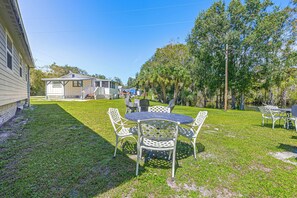 A grassy backyard with a patio table and chairs, a small house with a porch, and trees in the background. - Riverside Retreat -Horse Creel Retreat Arcadia (Arcadia)