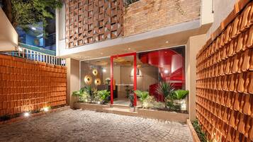 Entrada de hotel con fachada de ladrillo, puerta de vidrio con marco rojo y un muro de ladrillo con diseño geométrico.