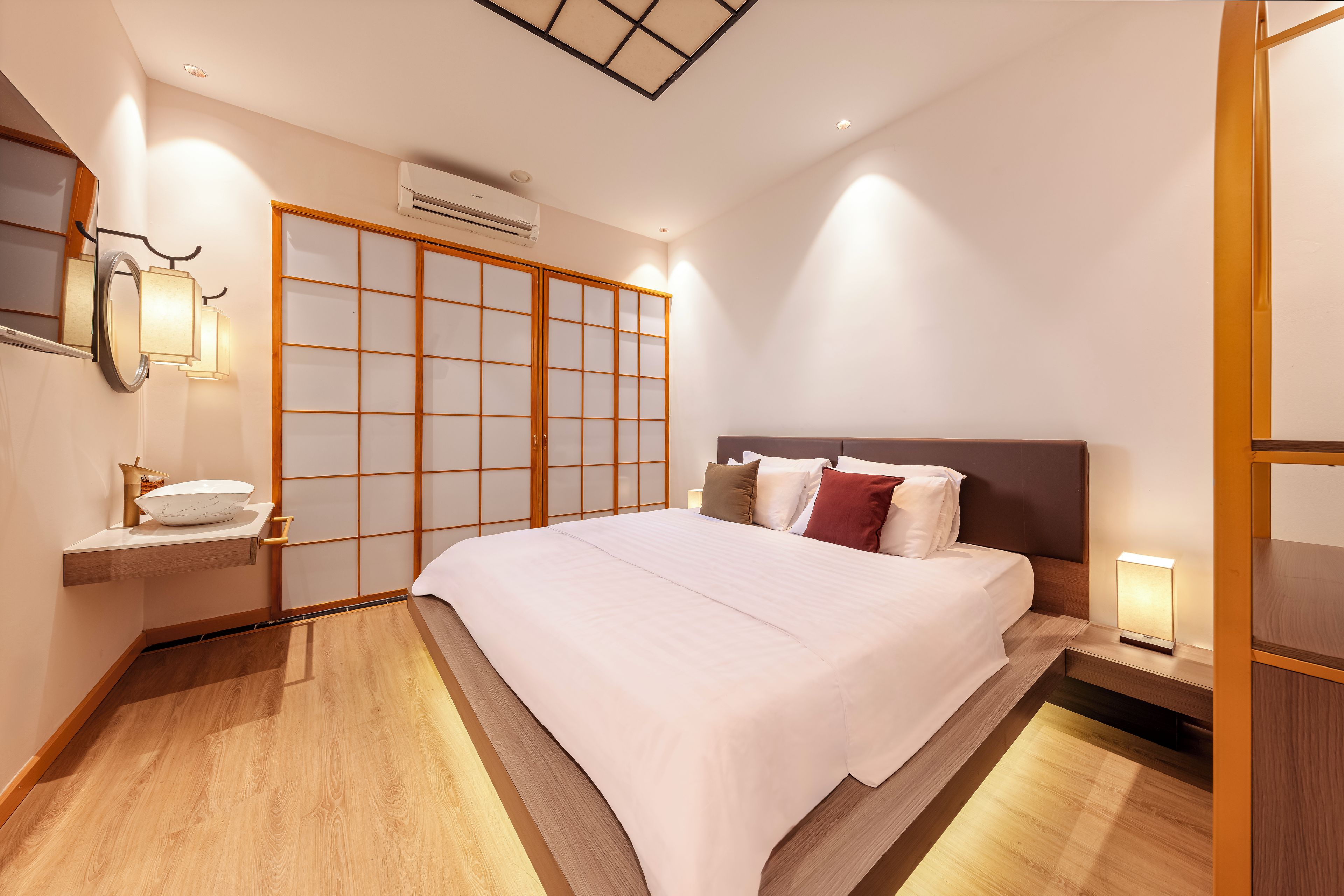 Una habitación de hotel con cama, mesita de noche, lámpara y un panel corredizo estilo shoji.