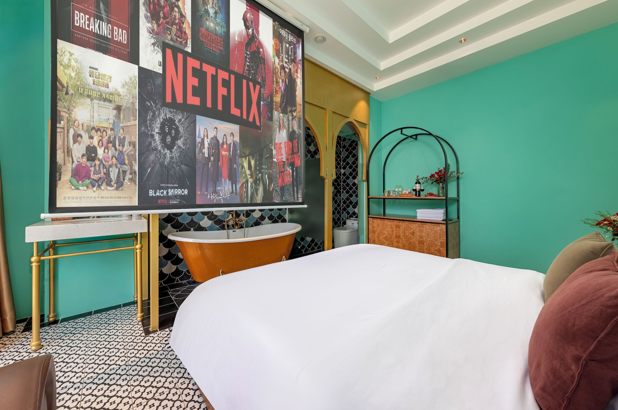 Ein Hotelzimmer mit einem großen Poster von Netflix-Filmen, einer Badewanne, einem Bett und einem Ablagefach mit Pflegeprodukten.