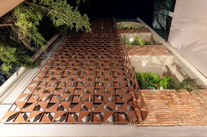 Una valla metálica con un diseño geométrico, un sendero de ladrillo y follaje.