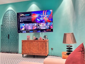 Una habitación con pared verde azulada, un armario de madera, un televisor que muestra una carrera y una lámpara.