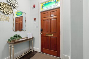 A wooden door with a brass handle, a mirror above it, and a welcome sign on a wooden console table with a plant. - Historic Old Town Retreat | Steps to King Street (Alexandria)