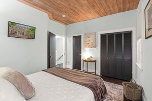A bedroom with a bed, a wooden ceiling, a door, a wall-mounted picture, and a dark door. - Historic Old Town Retreat | Steps to King Street (Alexandria)