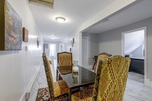 A dining area with a glass-top table and patterned chairs, a marble floor, and a hallway leading to a bedroom. - Extended Springfield Stay Near Downtown & MGM (Springfield)
