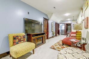 Una sala de estar con televisor, sofá, reposapiés y una mesita de noche con lámpara.