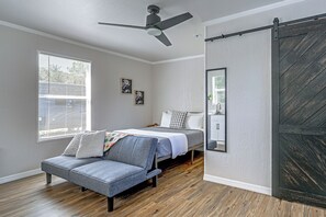 A bedroom with a bed, a chair, a ceiling fan, a window with blinds, and a sliding door.