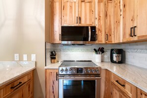 A kitchen with wooden cabinets, a stainless steel stove, a microwave, and a coffee maker. - NEW | 3 Mi to Whitefish Mountain | Ski + Snowshoe | Cedar Home, Stone Fireplace, Sleeps 8 (Whitefish)