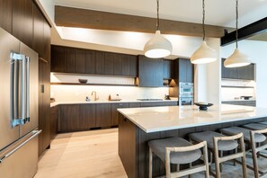 A modern kitchen with dark wood cabinets, stainless steel appliances, and a central island with bar seating. - New! Family Ski Getaway with Hot Tub, Chef's Kitchen & Fireside Deck, Monthly Stays (Whitefish)