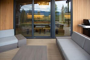 Un interior moderno con piso de madera, un amplio ventanal corredero que da a un espacio de comedor exterior y una zona de estar con sofá y mesa.