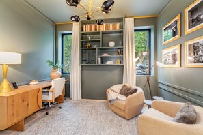 A cozy room with a desk, chair, bookshelf, and a comfortable seating area with a view of greenery outside. - New! Family Ski Getaway with Hot Tub, Chef's Kitchen & Fireside Deck, Monthly Stays (Whitefish)