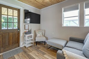 Un salon chaleureux avec une porte en bois, un téléviseur fixé au mur, un fauteuil à rayures, un banc et une fenêtre avec des stores.