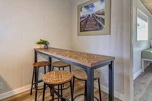 Un coin cuisine avec une table en bois et des tabourets de bar, une plante en pot et un tableau accroché au mur.