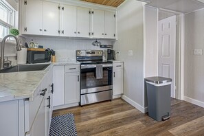 A modern kitchen with white cabinets, stainless steel appliances, and a wooden floor. - Cozy Creekside Cottage at Horse Creek Retreat (Arcadia)