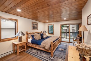A bedroom with a wooden bed, a nightstand, a lamp, a rug, and a glass container with corks. - New Listing! Ski-In/Ski-Out with Indoor Hot Tub in Big Sky (Big Sky)