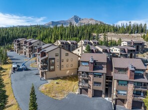 A residential area with multi-story buildings, a parking lot, and a mountain in the background. - New Listing! Ski-In/Ski-Out with Indoor Hot Tub in Big Sky (Big Sky)