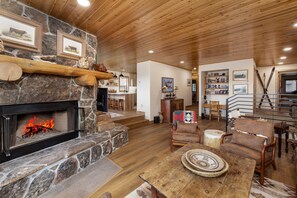 A cozy living room with a stone fireplace, wooden ceiling, and a dining area with a wooden table and chairs. - New Listing! Ski-In/Ski-Out with Indoor Hot Tub in Big Sky (Big Sky)