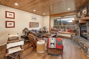 A cozy living room with a fireplace, wooden furniture, and framed pictures on the walls. - New Listing! Ski-In/Ski-Out with Indoor Hot Tub in Big Sky (Big Sky)