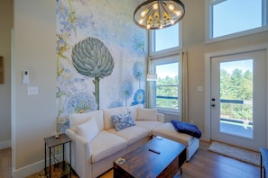 A living room with a white sofa, a wooden coffee table, a wall mural, and a large window with a view of trees. - Near Trails & Live Music! Quiet Floyd Gem w/ Views (Floyd)