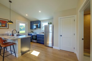 A modern kitchen with a central island, bar stools, and a view of the adjacent living area. - Near Trails & Live Music! Quiet Floyd Gem w/ Views (Floyd)