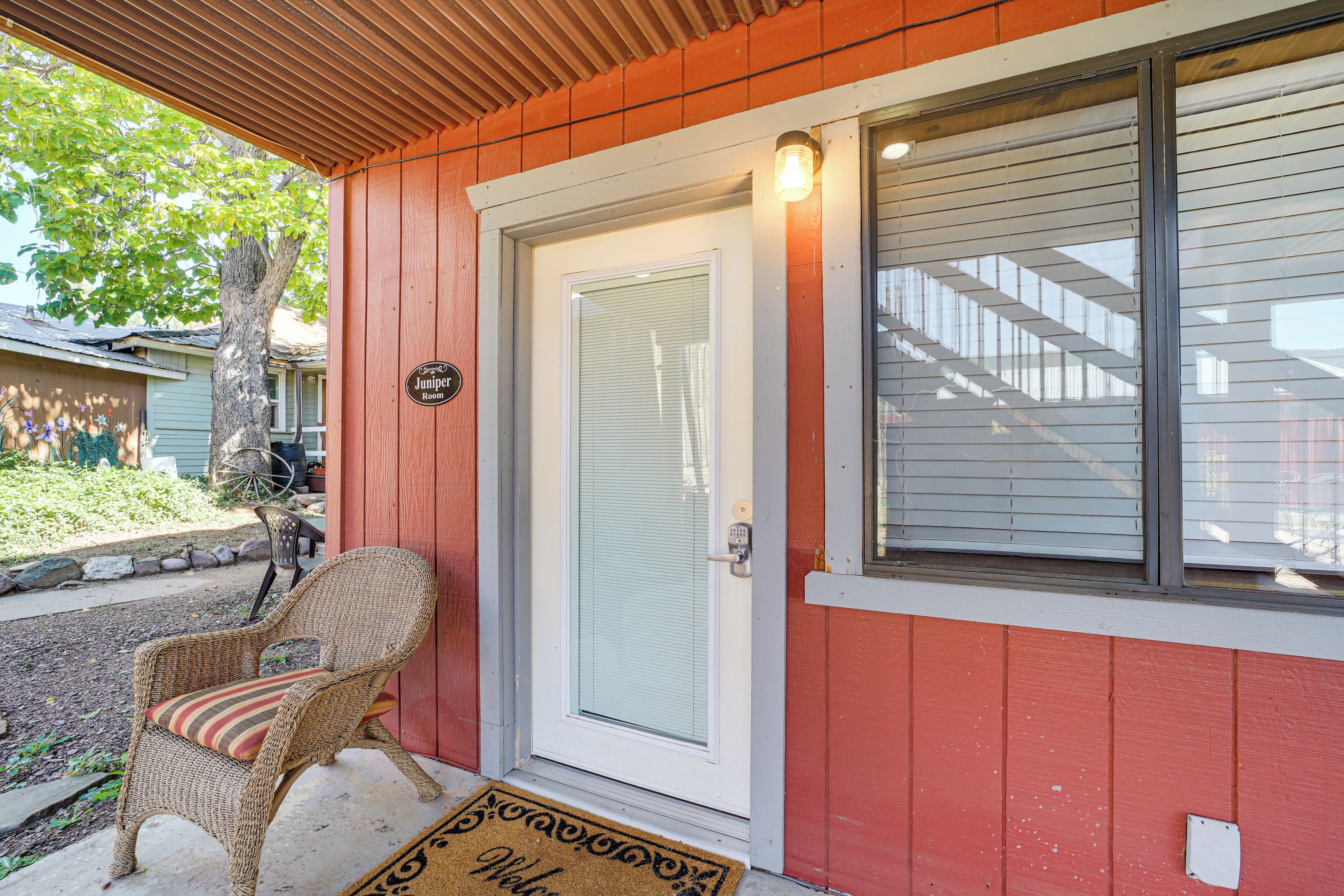 A wooden exterior with a red door, a wicker chair, and a doormat.