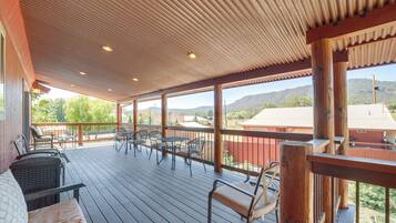 Une terrasse extérieure couverte, dotée d’un plancher en bois, de chaises et de tables en métal.