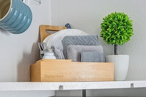 A wooden box labeled 'Thomas Grace Homewares' on a white shelf, containing kitchen utensils, a blue ceramic pot, and a green plant. - Otter Creek Cabin - Horse Creek Retreat Arcadia (Arcadia)