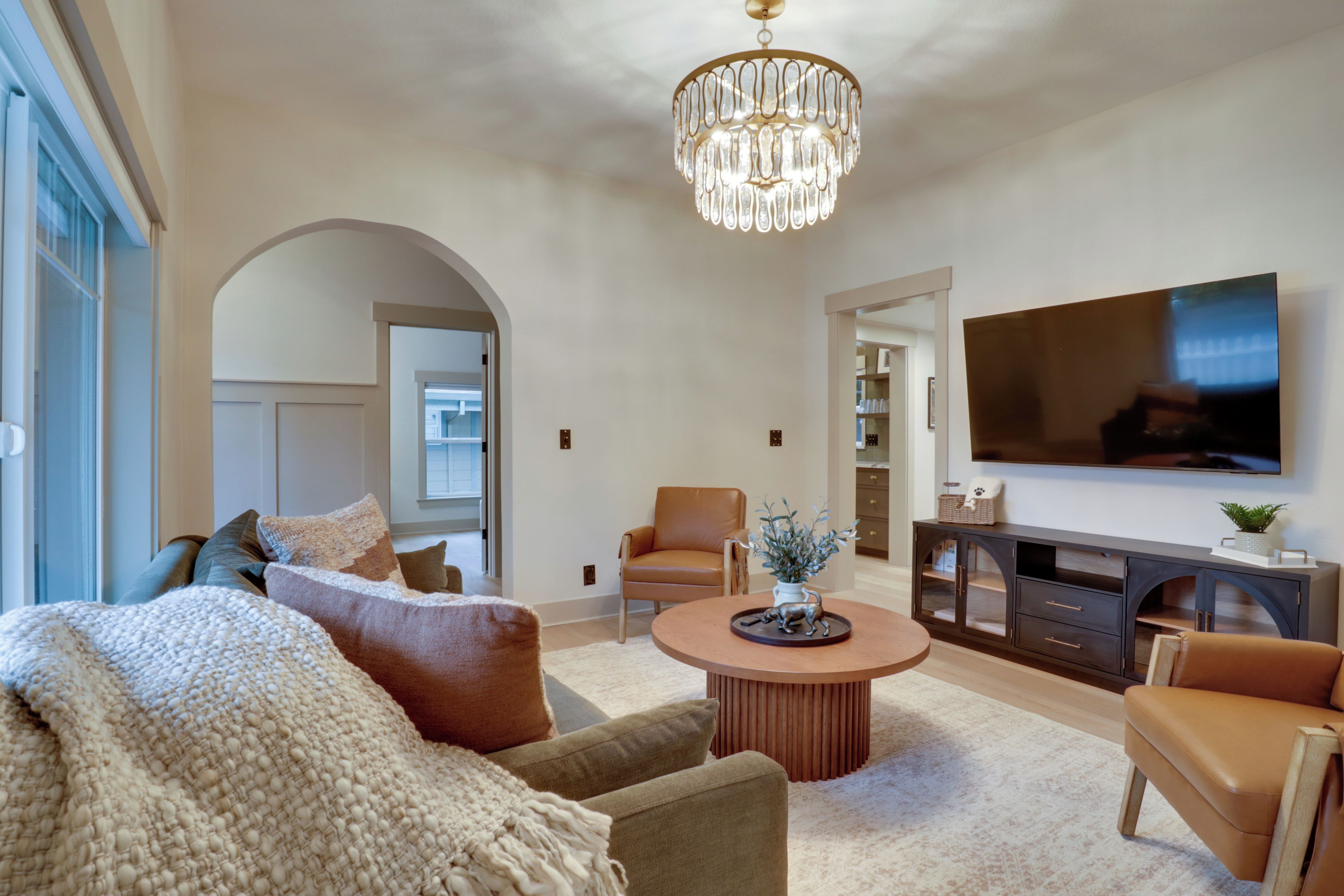 A modern living room with a large TV, comfortable seating, and a decorative chandelier.