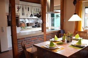 A dining area with a brick wall, wooden beams, and a window with yellow curtains. - Holiday home in Hooksiel with swimming pool (Hooksiel)