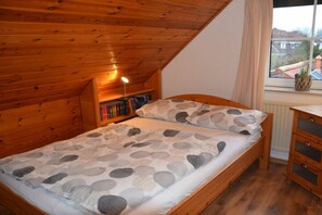Un dormitorio con techo inclinado, una cama de madera, una mesita de noche y un ventanal con vistas a casas.