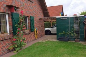 A brick house with a garden, a white car parked in the driveway, and a green fence. - Holiday home in Hooksiel with swimming pool (Hooksiel)
