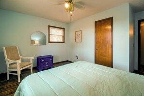 Quarto com cama, cadeira, penteadeira, porta e ventilador de teto.