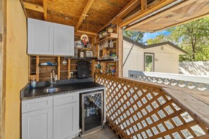 Een houten interieur met een keukenhoek, inclusief een gootsteen en kasten, en uitzicht op een klein huis.
