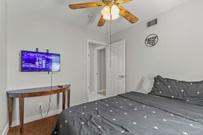A bedroom with a bed, a television on the wall, a ceiling fan, and a door leading to another room. - Home w/ Outdoor Entertainment Area in San Antonio! (San Antonio)