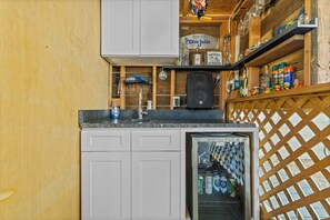A kitchen with a refrigerator, a sink, and a shelf with various items including a bottle of tequila and a speaker. - Home w/ Outdoor Entertainment Area in San Antonio! (San Antonio)